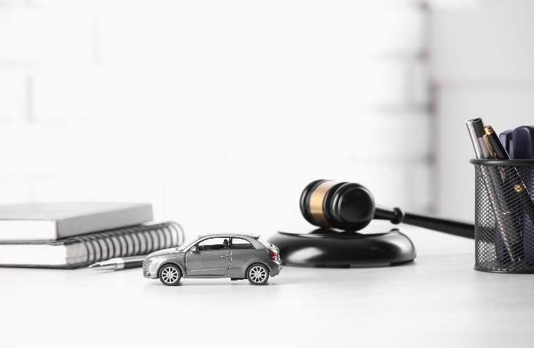 Toy car, judge's gavel and stationery on white table