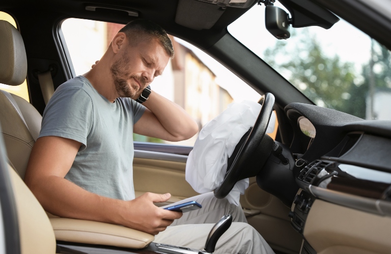 Injured man near opened airbag in automobile after car accident